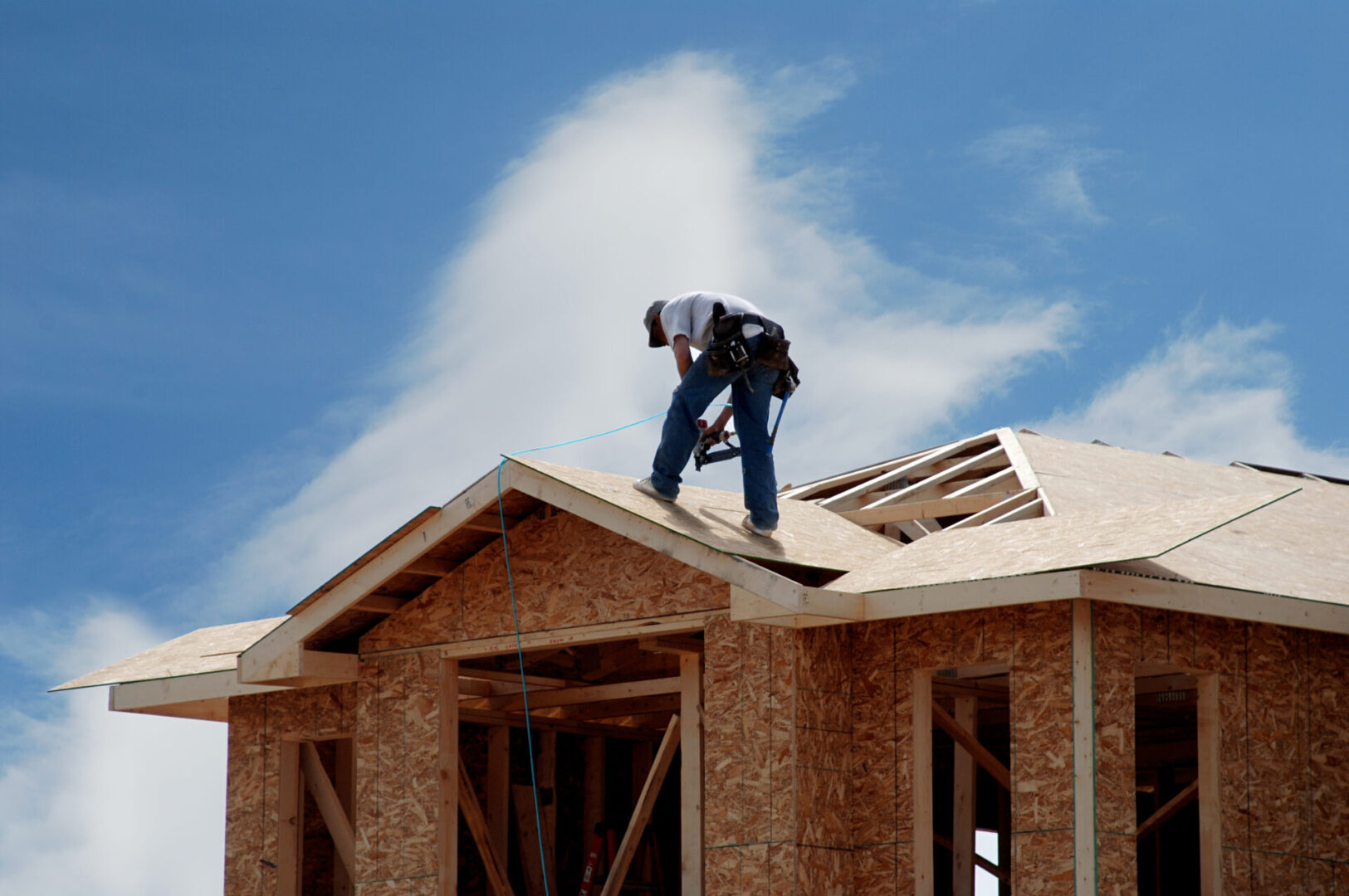 A construction worker on top of a roof wearing a harness Construction worker on a house roof.