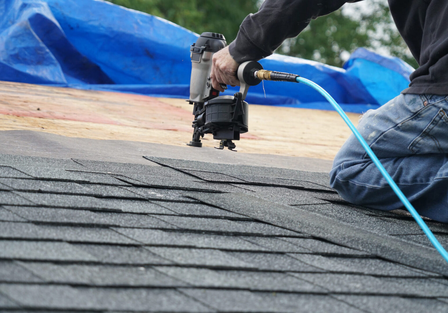 handyman using nail gun to install shingle to repair roof Roofer using nail gun on asphalt shingles.